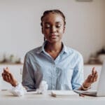 Coping With Stress At Work. Young African Businesswoman Meditating In Office